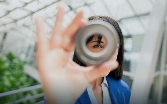 Frau schaut mit einem Auge durch ein metallenes rundes Objekt